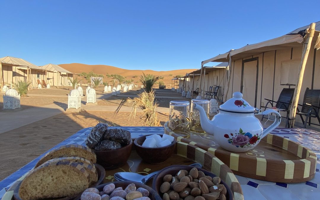 In the vast and breathtaking landscapes of the Moroccan desert, tea plays a central role in the expression of hospitality. As you traverse the golden dunes and immerse yourself in the tranquility of the desert, you'll encounter the warm and welcoming tradition of tea ceremonies that have been cherished for centuries. In the heart of the desert, where life flourishes against all odds, Berber nomads and local communities graciously invite travelers into their tents, sharing a cup of tea as a symbol of friendship and hospitality. This age-old ritual offers a glimpse into the genuine warmth and generosity of the desert dwellers. Mint tea, commonly known as "Moroccan whiskey," takes center stage in these desert hospitality rituals. The delicate aroma of fresh mint leaves fills the air as the tea is meticulously prepared. Green tea leaves, preferably gunpowder tea, are carefully steeped with sprigs of mint and an appropriate amount of sugar, creating a harmonious blend of flavors. As the tea brews, the pot is often swirled gently to infuse the flavors evenly. Once the tea has reached its desired strength, it is ceremoniously poured into small, beautifully adorned glasses from a considerable height, creating an impressive stream of tea that aerates and cools it down. The pouring itself is an art form, showcasing the host's skill and hospitality. Sipping on a glass of mint tea in the serene desert setting, you'll feel a sense of tranquility and connection to the surroundings. The combination of the aromatic mint, the sweetness of the sugar, and the earthy undertones of the tea create a delightful sensory experience. This traditional tea ceremony is not merely a drink but a cultural experience that fosters connections between people. It is a moment to slow down, savor the flavors, and engage in meaningful conversations. The act of sharing tea in the desert becomes a bridge between strangers, breaking down barriers and creating lasting memories. So, as you venture into the Moroccan desert, be prepared to immerse yourself in the ritual of tea. Embrace the warmth of the hospitality offered by the desert nomads and local communities, and let the flavors of mint tea transport you into a world of genuine connection and shared experiences.