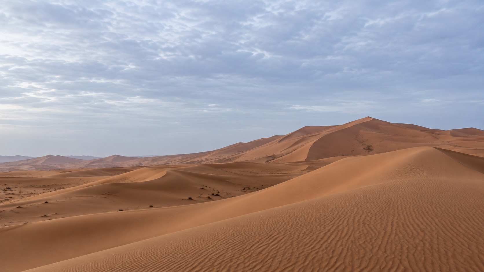 Sweeping Sahara sand dunes beneath a softly clouded sky